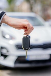 Close-up of a hand holding a car key, with a white car in the background outdoors.